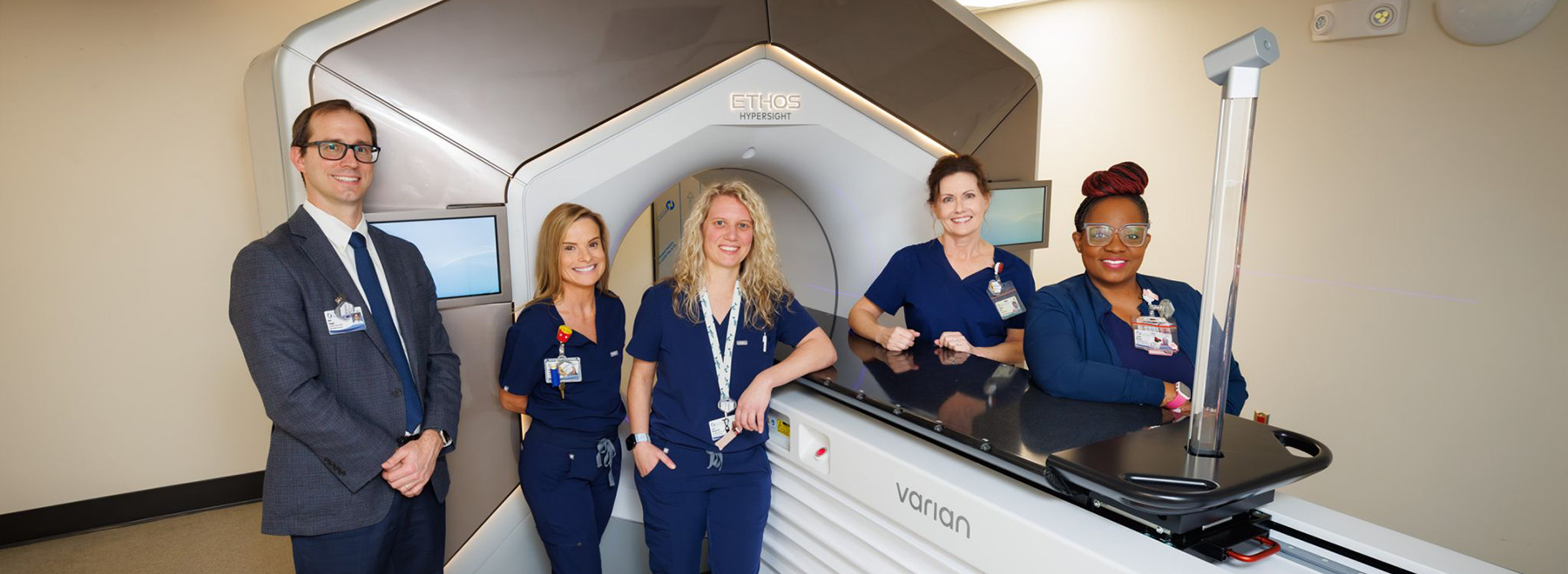 Six healthcare staff stand beside an Ethos Hypersight medical imaging machine with a treatment table in a clinic room.
